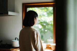 Woman gazes out of a sunlit kitchen window surrounded by greenery in the afternoon light photo