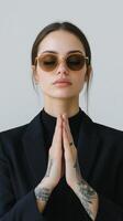 Confident woman in sunglasses and a black suit poses with hands together in a stylish indoor setting photo