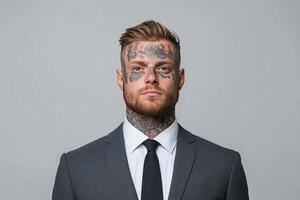 Man with tattoos dressed in a suit poses confidently against a gray backdrop photo