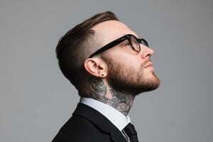 Stylish man with tattoos and glasses poses confidently in a suit against a plain background photo