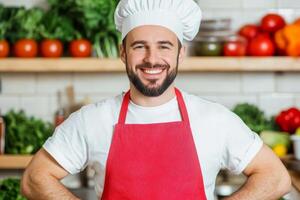 Chef in a kitchen smiles while wearing an apron and hat with fresh vegetables in the background during daytime cooking preparation photo