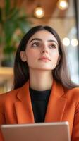 Young woman in orange blazer contemplating future in modern cafe during afternoon photo