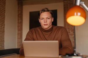 Focused young man working on a laptop in a cozy office space during the day photo