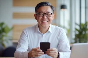 Man sitting in a modern cafe smiling while holding a smartphone during daytime photo