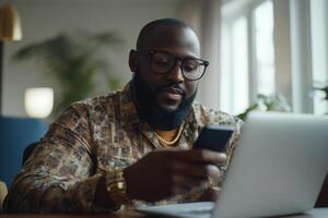 Man in patterned shirt using smartphone while working on laptop in a cozy indoor environment photo