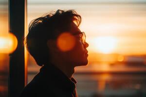 Silhouette of a man gazing at a sunset through a window in a modern urban setting during evening hours photo