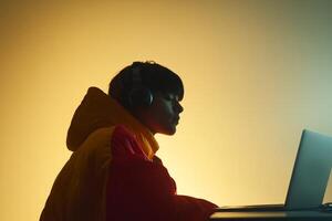 Young person wearing headphones focused on laptop in a colorful setting during evening hours photo