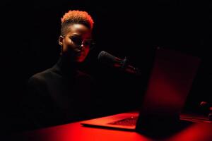 A focused person wearing sunglasses interacts with a laptop while speaking into a microphone. photo