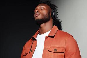 Young man enjoying music while wearing headphones in stylish orange jacket against a contrasting background photo