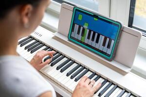 Close up view of young woman learning to play the keyboard at home using an interactive app. Using mobile apps for self-study concept. High quality photo