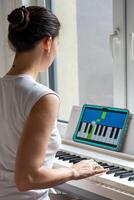 Young woman learning to play the keyboard at home using an interactive app. Using mobile apps for self-study concept. High quality photo