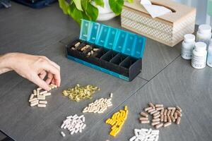 Close up view of Man hand sorting his pills and supplements into a weekly pill organizer. Concept of medication management and daily health routine. High quality photo