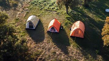 Beautiful aerial view of camping tents set up on a green meadow, illuminated by the warm glow of a sunset photo
