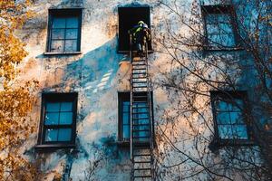 A determined fireman climbing a ladder to rescue or control a fire on the wall of a building in the city, showcasing action and bravery photo