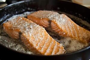 A close-up shot of fresh salmon fillets being fried in a frying pan. The golden, crispy texture of the fish contrasts beautifully with its rich photo