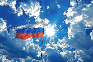 The Russian flag proudly waves in the breeze against a bright blue sky, with the sun shining in the background. The vibrant colors of the flag contrast beautifully with the clear sky. photo