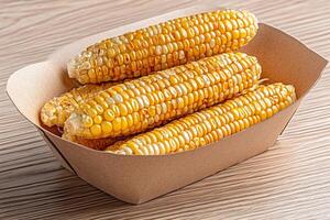 Grilled corn cobs resting in a cardboard container on a wooden table photo