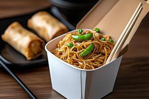 Noodles with chicken and peas in takeaway box with spring rolls and chopsticks photo