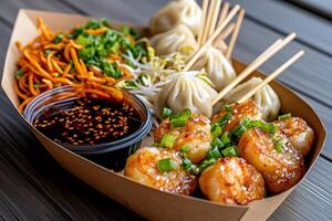 Delicious asian food box with fried shrimps, dim sum, soy sauce, carrot noodles and bean sprouts photo