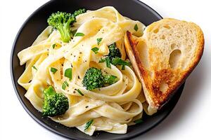 Fettuccine alfredo pasta with broccoli florets and toasted bread in black bowl photo