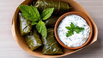 Dolmas with yogurt sauce, garnished with fresh mint and parsley, served in a takeaway container photo