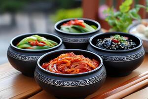Four black bowls containing different kinds of kimchi resting on wooden table photo