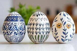 Three easter eggs with hand-painted floral and geometric patterns standing on white table photo