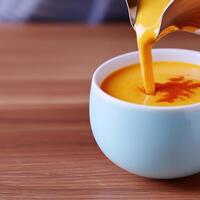 A person pouring orange soup into a cup photo