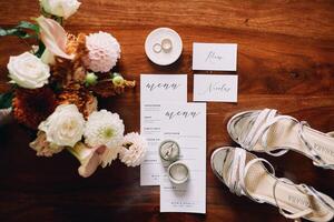 Amsterdam, Netherlands - June 5, 2024. Bride shoes stand on a wooden table next to the invitations and a bouquet of flowers. Top view photo