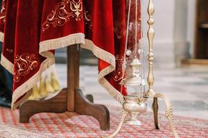 Smoking censer hangs on a gold chain on a stand near a table with a red tablecloth photo