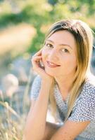 Smiling girl sits in the grass, resting her head on her hand photo