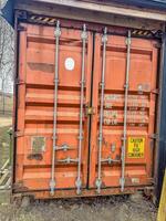 Orange shipping container with warning sign near rural area, showcasing cargo details and safety information on a clear day. High quality photo