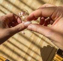 Close-up of hands applying nude-colored press-on nails on a wooden surface. High quality photo