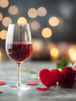 A glass of red wine and a rose on a table with a blurry background photo