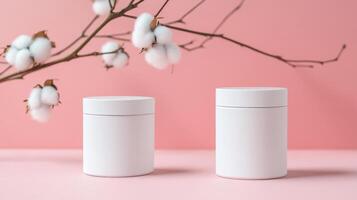 two white jars for cream on a pink delicate background with cotton branch. mockup for cosmetics, spa products photo