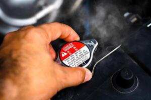 Hand removing the radiator cap from a car radiator while the radiator coolant overheated , Car repair concept photo