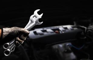 Mechanic holding wrenches during engine maintenance in automotive workshop photo