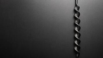 Twisted Black Drill Bit Against a Smooth Dark Textured Surface photo