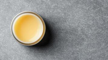 Open Jar of Creamy Yellow Substance on a Speckled Gray Stone Surface photo
