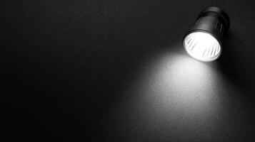 Illuminated Black Flashlight Casting a Bright Beam on a Dark Surface photo