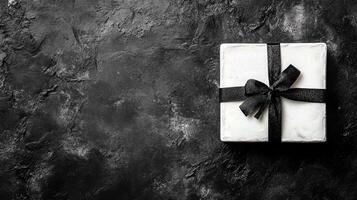 White Gift Box Wrapped with a Black Ribbon Bow on a Dark Stone Surface photo