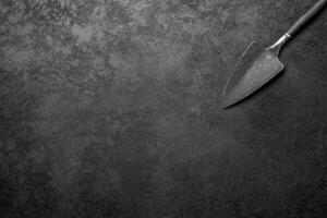 Worn Metal Trowel with a Wooden Handle on a Dark Textured Surface photo