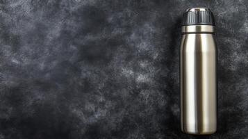 Sleek Silver Water Bottle with a Black Cap on a Dark Textured Surface photo