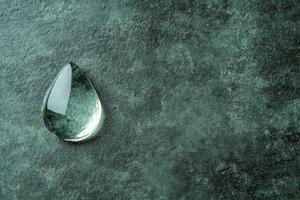 Clear Glass Droplet on a Textured Green Stone Surface photo