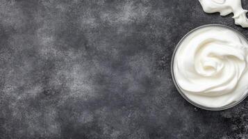 Swirled White Cream in a Glass Container on a Dark Textured Stone Surface photo
