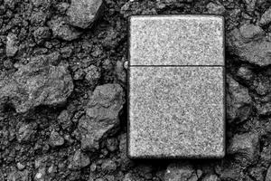 Shiny Rectangular Igniter Amidst Craggy Black Stones in Grayscale photo
