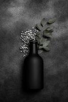 Black Bottle with Green Leaves and White Flowers on a Textured Dark Surface photo