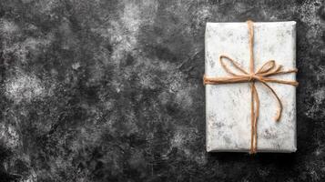 White Gift Box with Twine Bow on a Textured Dark Gray Surface photo