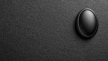 Black Oval Button on a Textured Dark Gray Surface in Monochrome photo