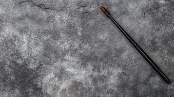 Black Mascara Wand with Brown Bristles on a Textured Gray Surface photo